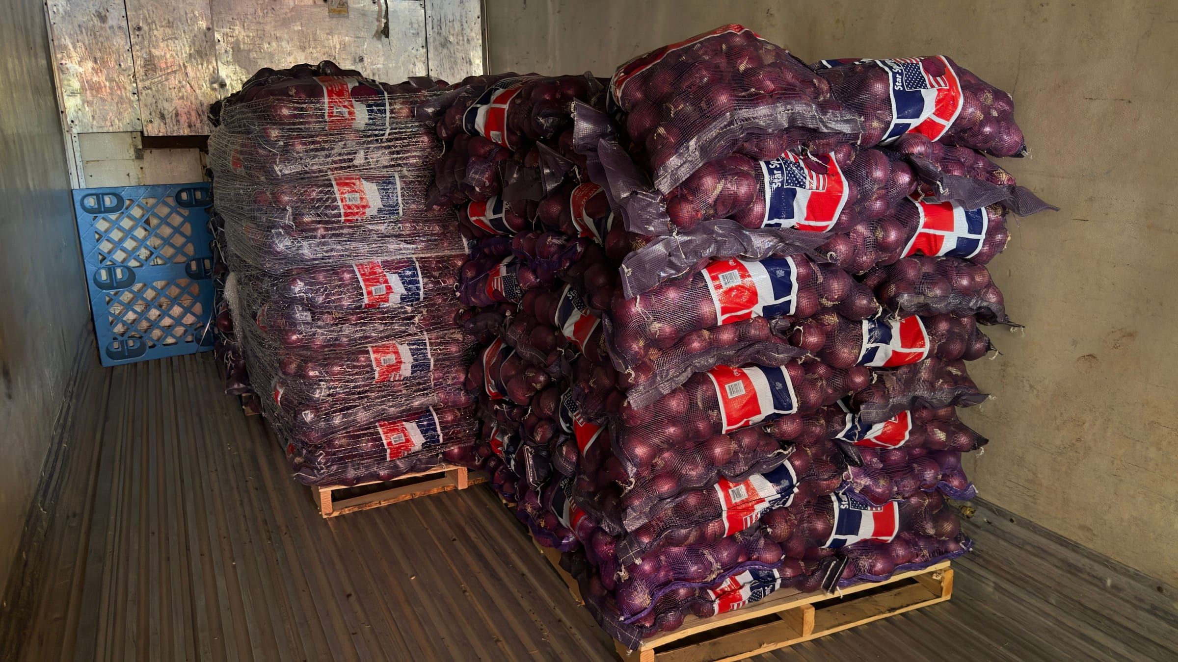 Tarimas de cebolla morada estadounidense en sacos de 50 lb con etiquetas de bandera de EE. UU. dentro de un tráiler