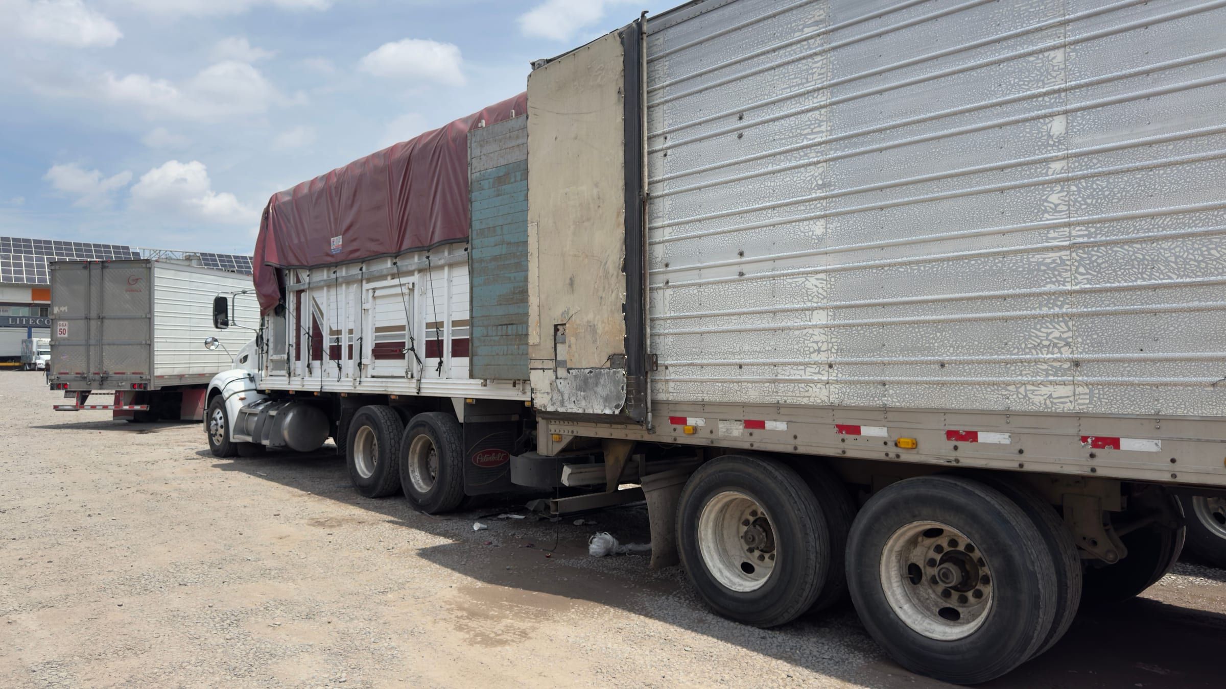 Un tráiler refrigerado estadounidense estacionado junto a un camión mexicano con lona, en trasbordo de producto
