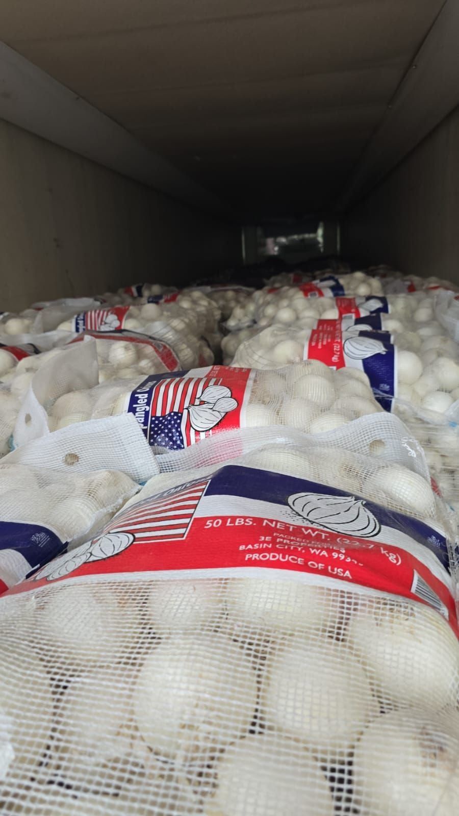 Sacos de malla de cebolla blanca estadounidense con etiquetas Produce of USA estibados dentro de un tráiler